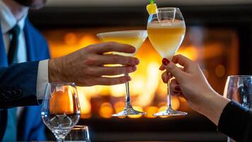 Two people toasting with champagne glasses in a warmly lit room with a fireplace in the background.