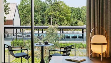 A modern room with a view of a pool and greenery. It includes a table with chairs, a lamp, and a book.