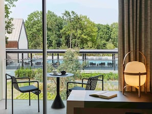 Une chambre moderne avec vue sur une piscine et un espace verdoyant. Elle comprend une table avec des chaises, une lampe et un livre.