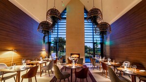 A modern dining area with round tables, chairs, and hanging light fixtures. - Le Domaine des Vanneaux Golf & Spa L'Isle Adam - MGallery Collection (Presles)