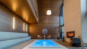 A modern indoor swimming pool with a wooden ceiling, a seating area with chairs, and a fireplace. - Le Domaine des Vanneaux Golf & Spa L'Isle Adam - MGallery Collection (Presles)