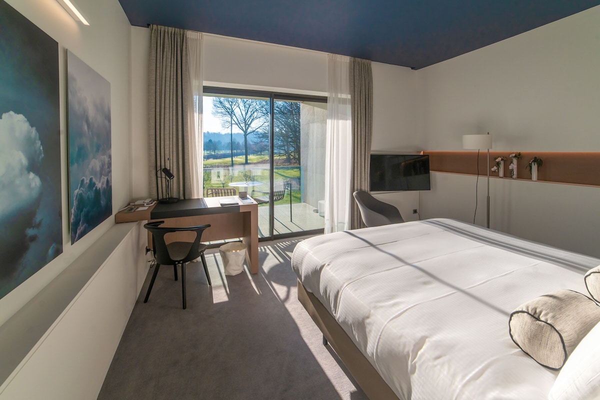A hotel room with a bed, desk, chair, and a TV.