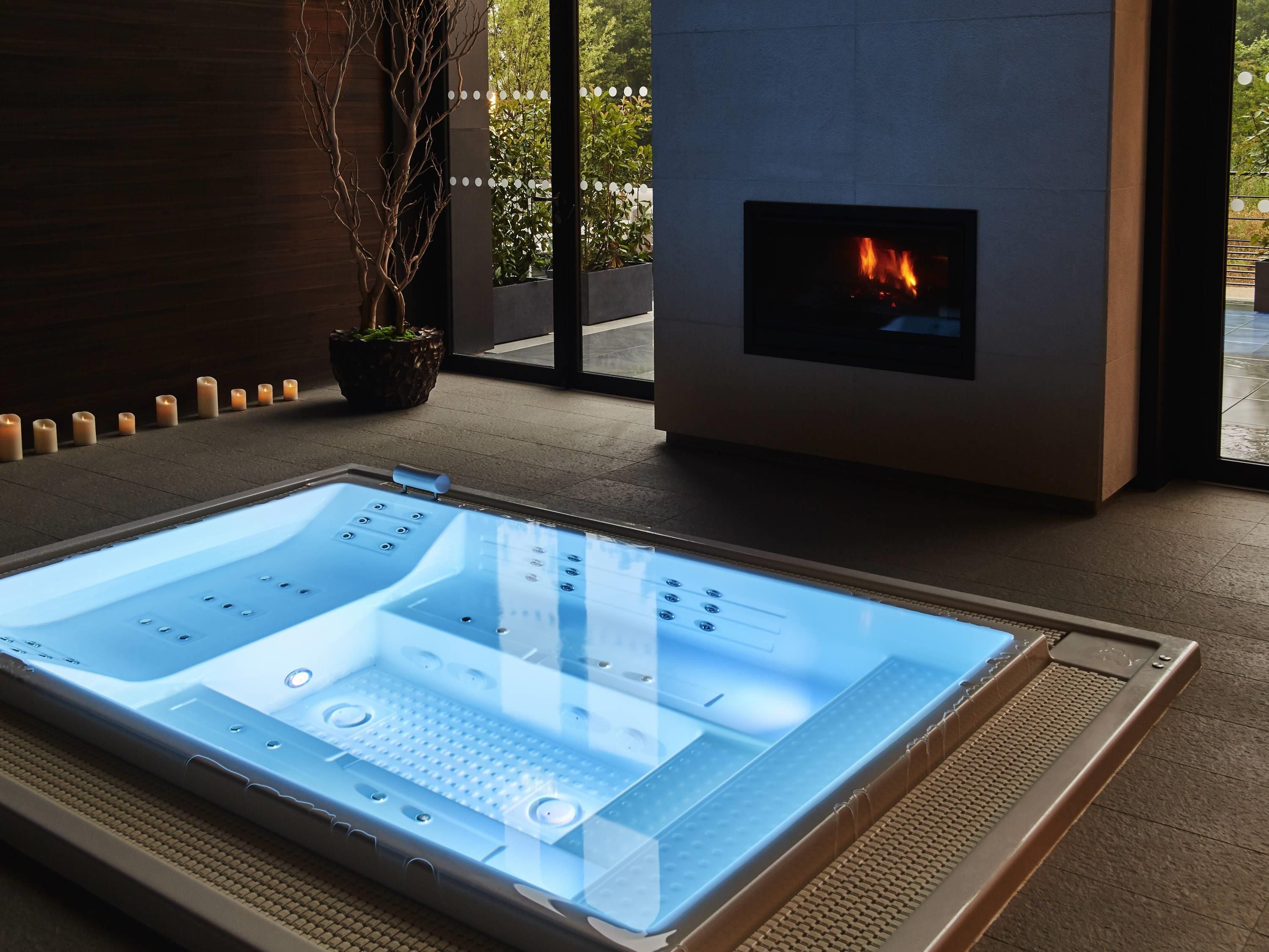 A modern spa room with a glass-enclosed hot tub, a fireplace, and a potted plant.