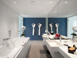 A modern bathroom with a large bathtub, a white sink, and a mirror. There are white towels and a potted orchid on the counter. - Le Domaine des Vanneaux Golf & Spa L'Isle Adam - MGallery Collection (Presles)