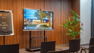 A conference room with a large screen displaying a hotel interior, wooden panel walls, and black chairs.