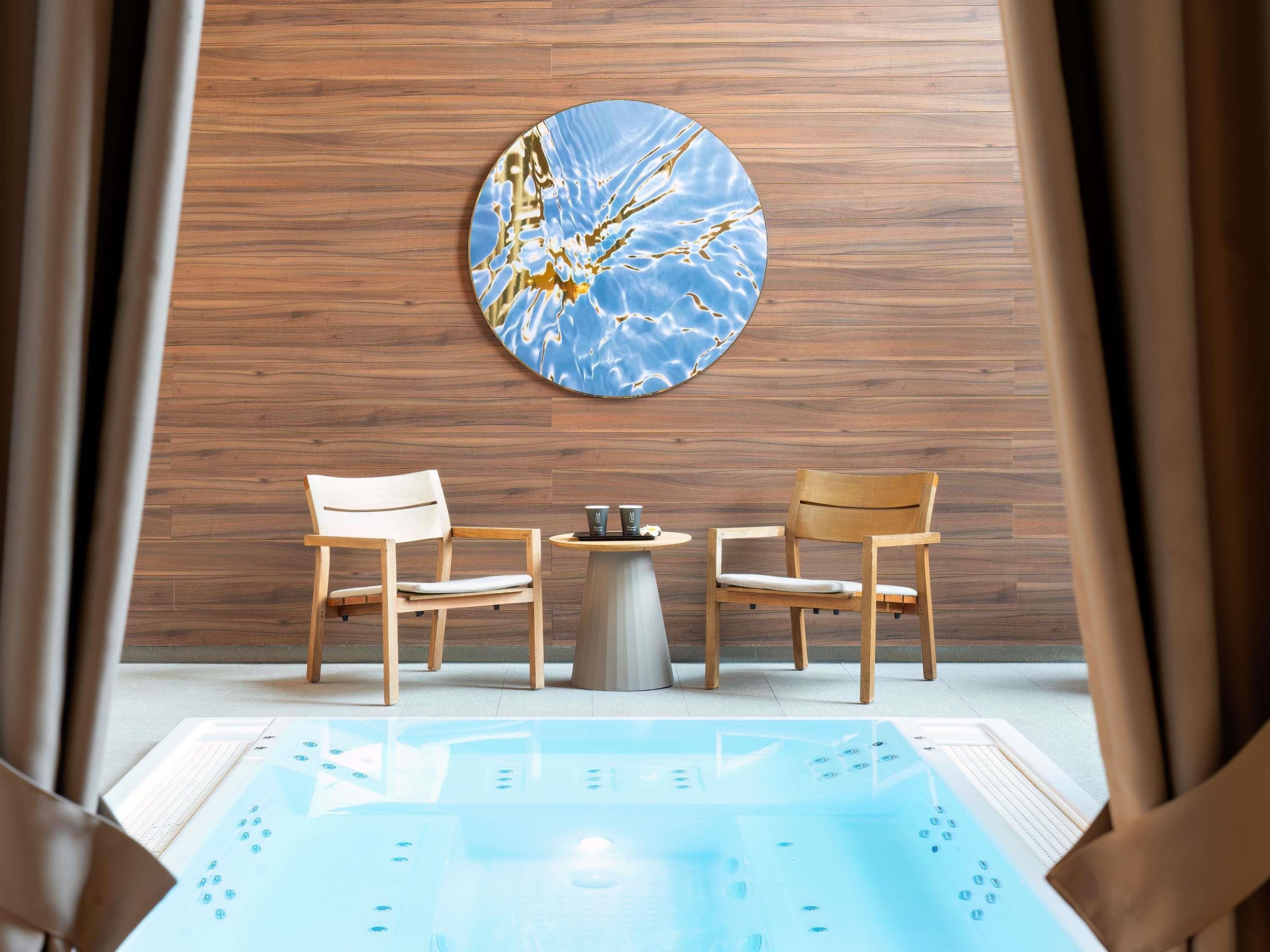 A spa room with wooden panel walls, two wooden chairs, a small round table with a coffee cup, and a large blue and gold artwork.