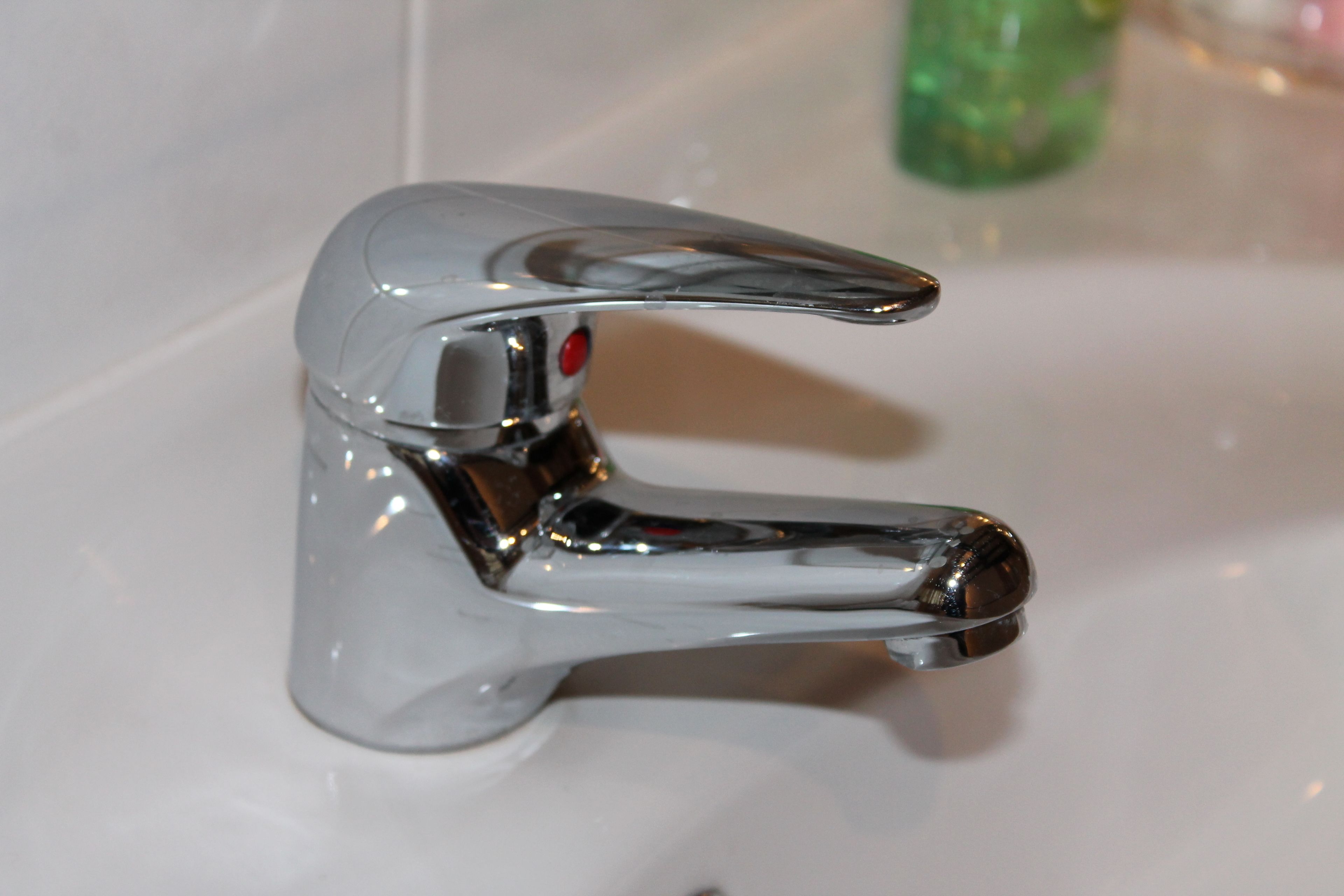 A chrome faucet with a red button, mounted on a white sink.
