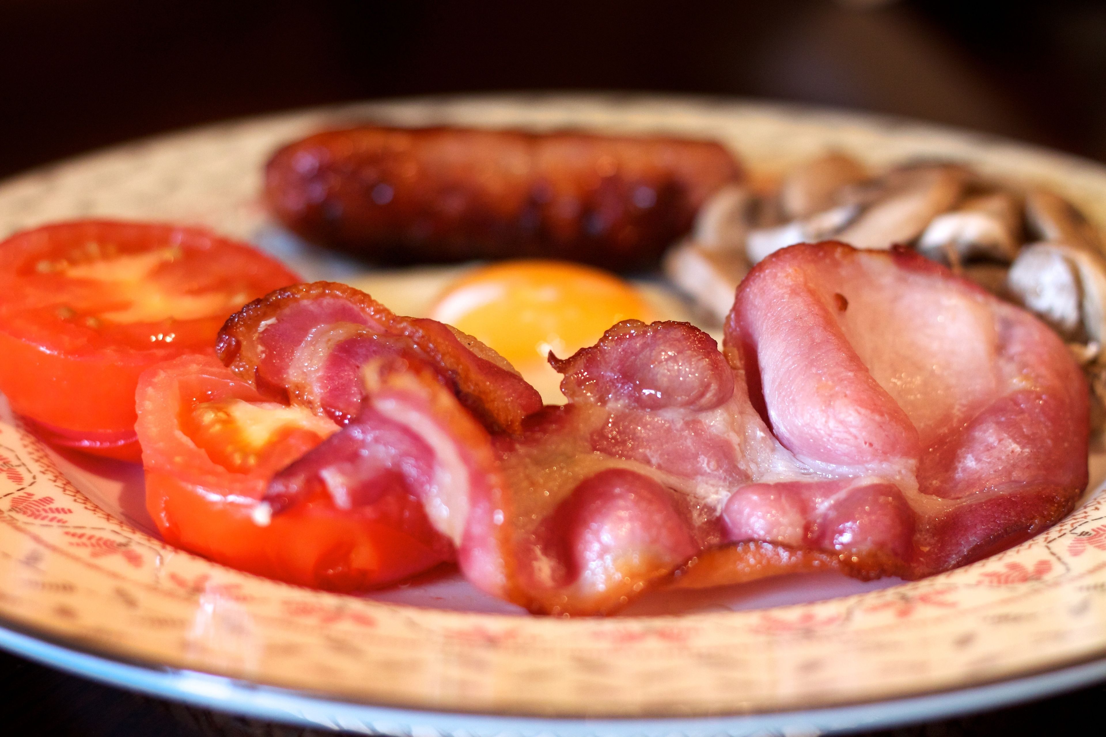 Une assiette de nourriture pour le petit-déjeuner comprenant du bacon, des saucisses, des œufs et des tomates.