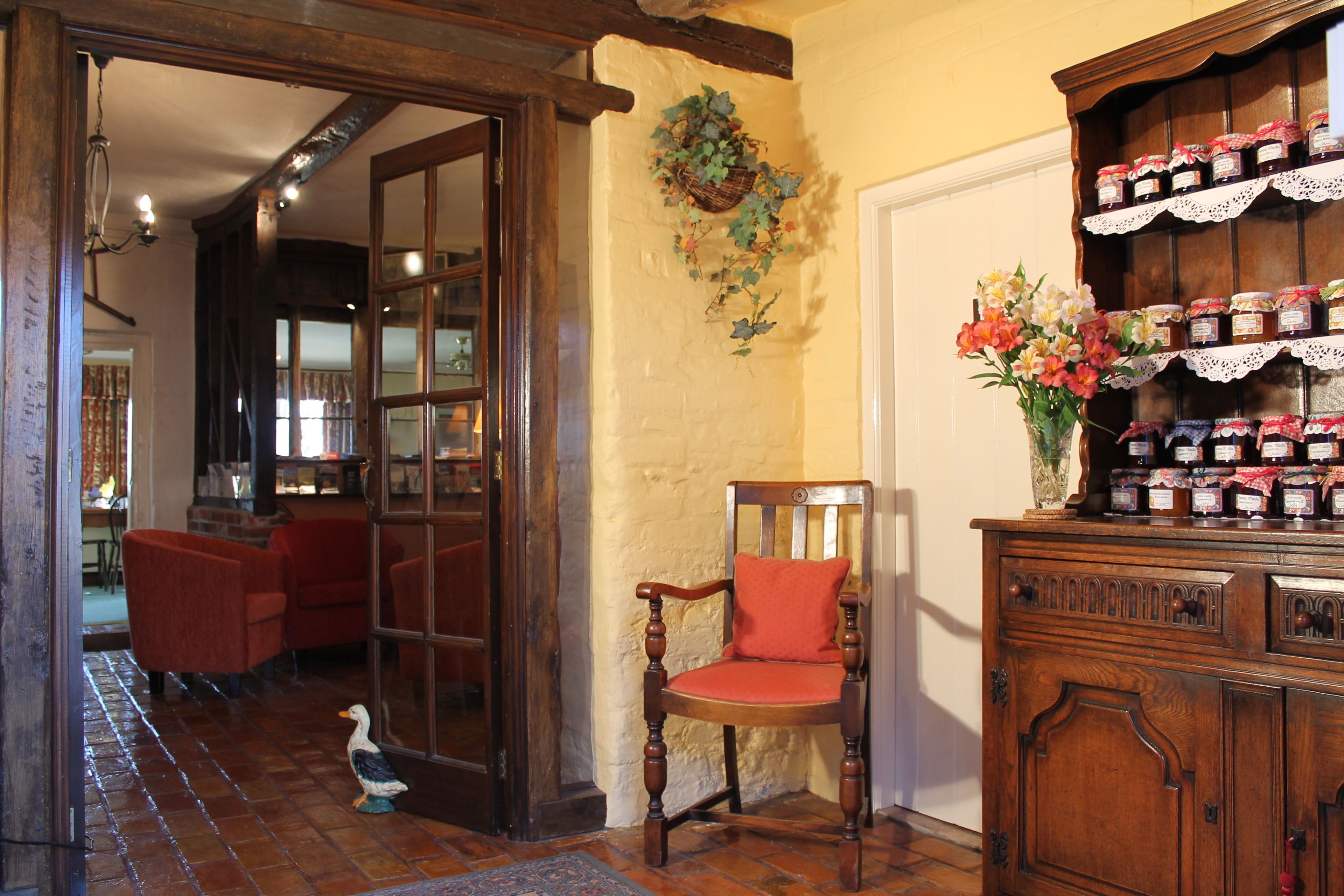 A wooden chair with a red cushion in a room with a tiled floor and a wooden cabinet with jars.