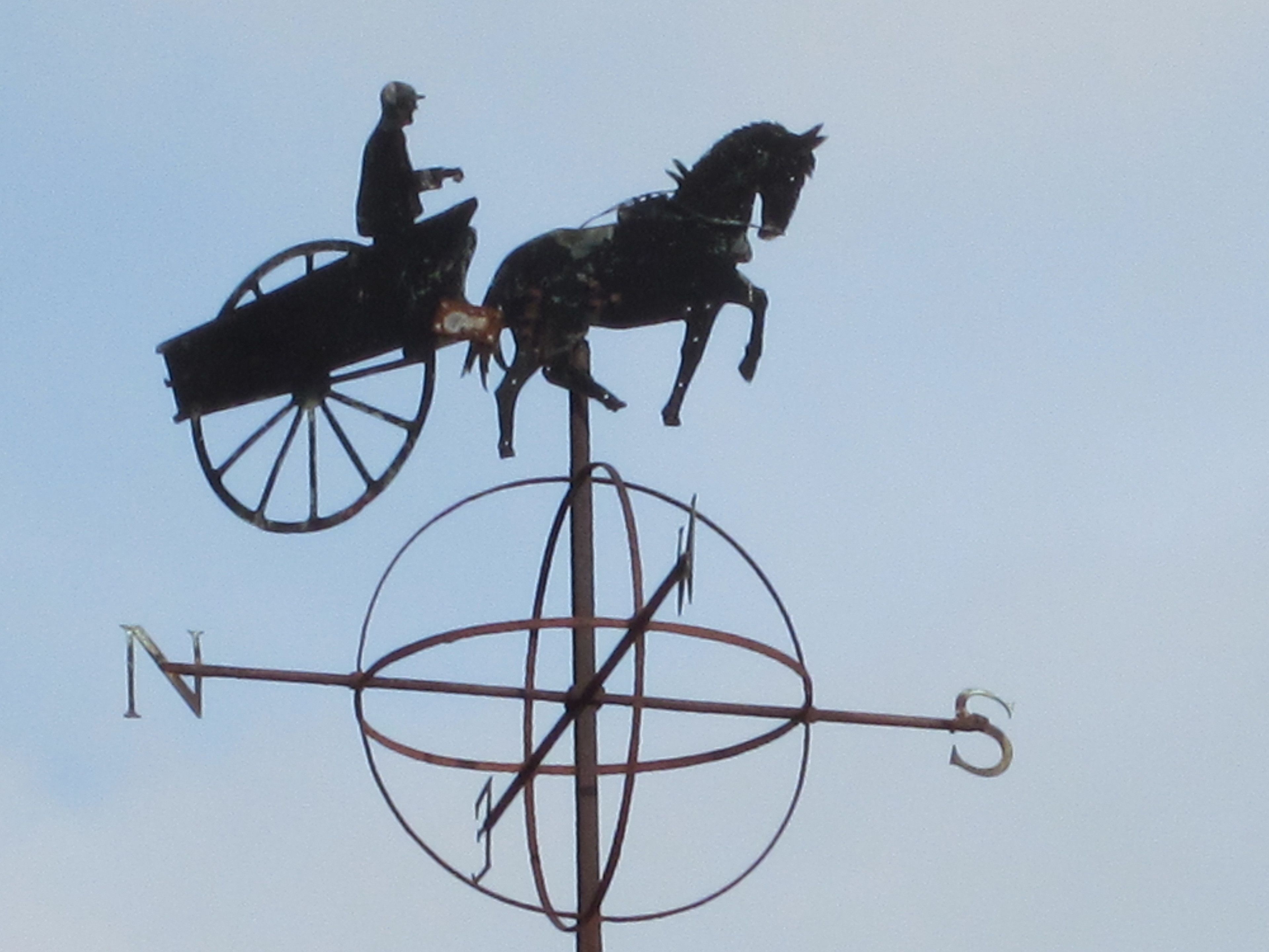 A weather vane with a figure on a horse-drawn carriage.