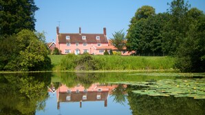 A large pink house with a reflection in a calm lake, surrounded by greenery. - Colston Hall Farmhouse B&B (Woodbridge)