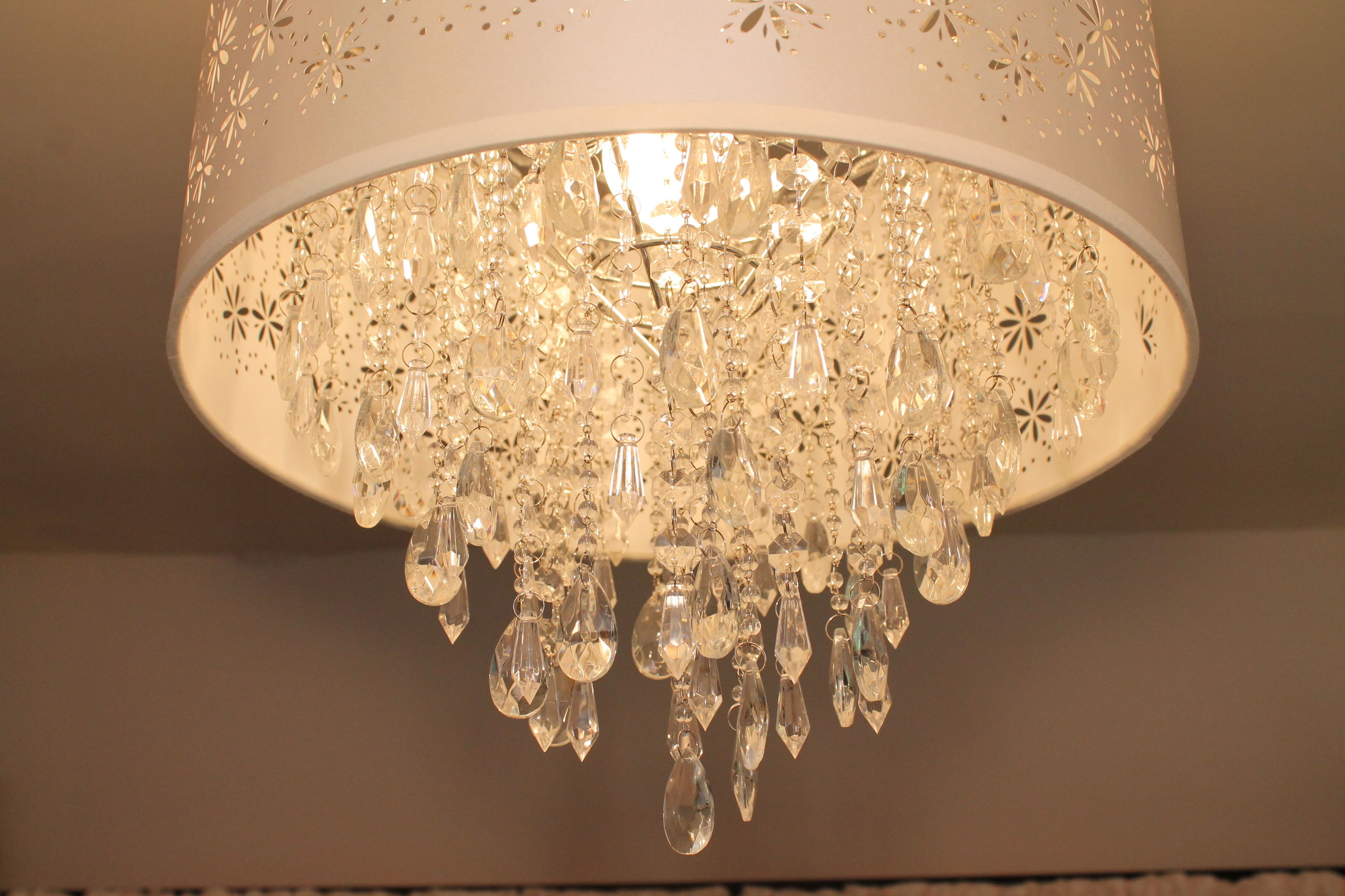 Un lustre composé de nombreux éléments de cristal suspendus à une structure métallique blanche perforée.