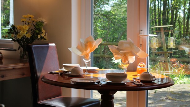 A dining table set with plates, bowls, and a vase of flowers. - Colston Hall Farmhouse B&B (Woodbridge)