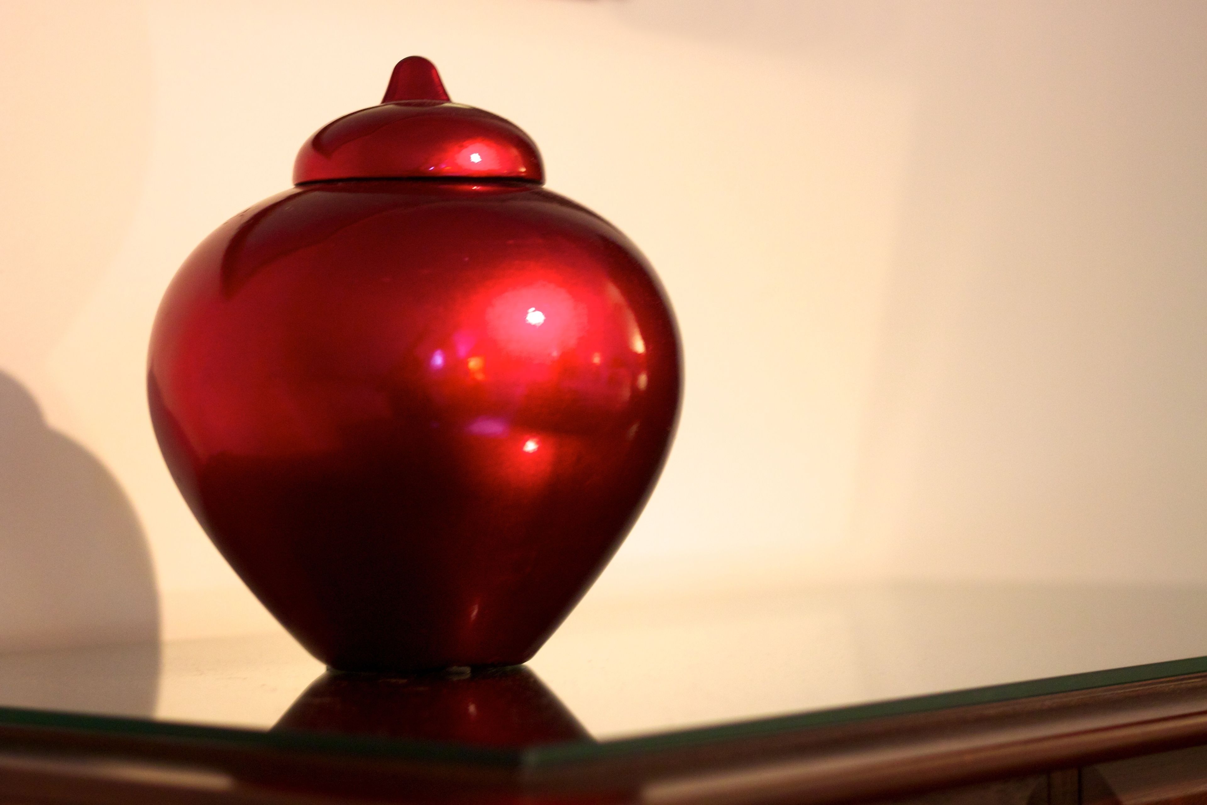 A red vase on a glass shelf.