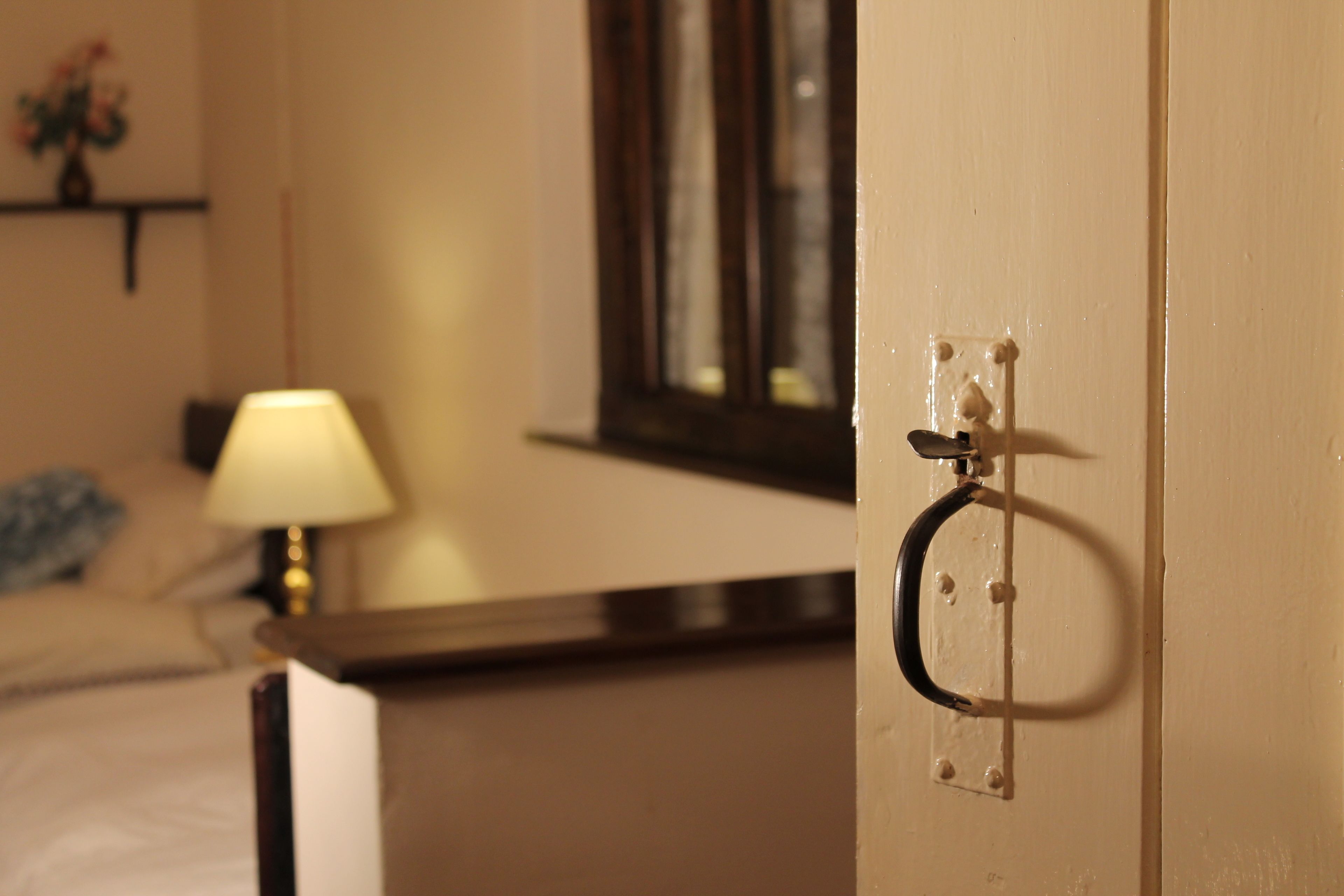 A hotel room with a bed, a bedside lamp, and a door with a handle.