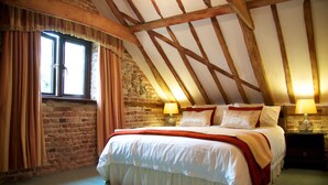 A bedroom with a large bed, wooden beams, brick walls, and two bedside lamps. - Colston Hall Farmhouse B&B (Woodbridge)