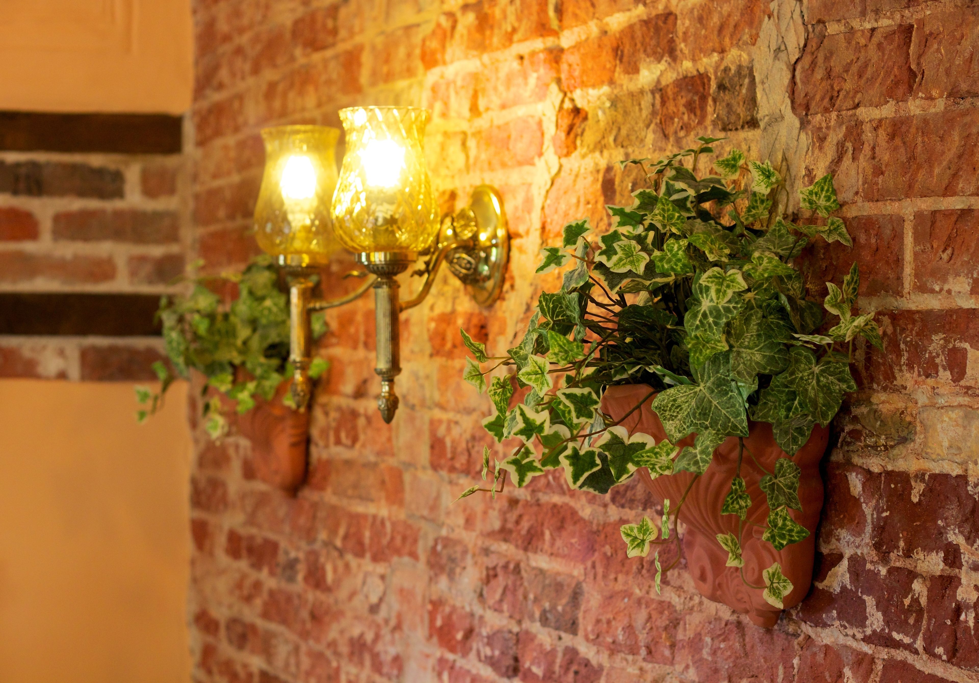 A brick wall with two wall-mounted lamps and a hanging planter with ivy.