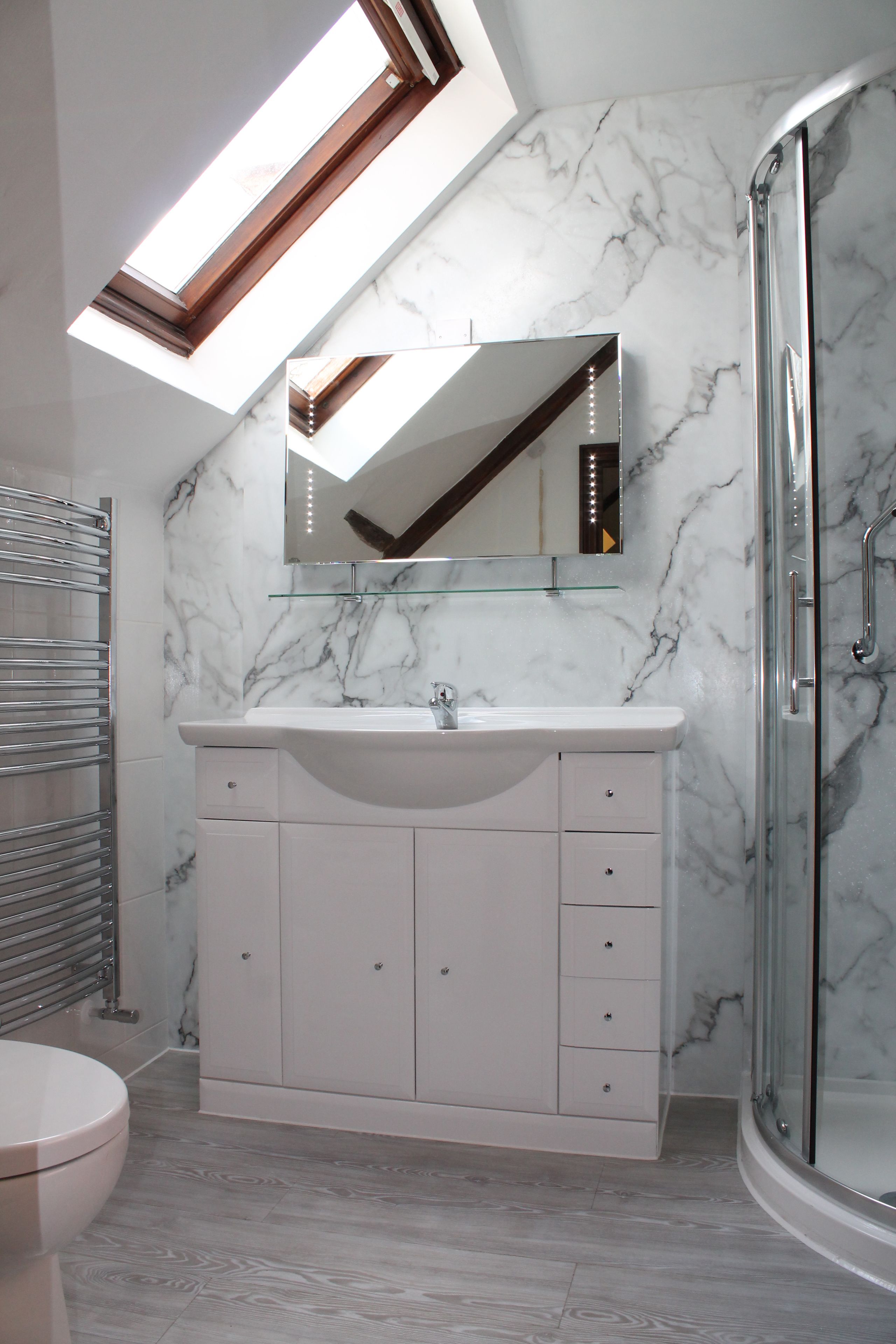 Un baño moderno con tragaluz, cabina de ducha de vidrio y salpicadero de mármol.