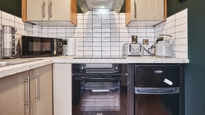 Una cocina compacta equipada con microondas, tostadora, hervidor y horno empotrado.