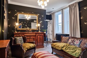 A room with a large mirror, a vanity with lights, a sofa with patterned cushions, and a view of the outdoors. - Snug at Clarence (Londonderry)