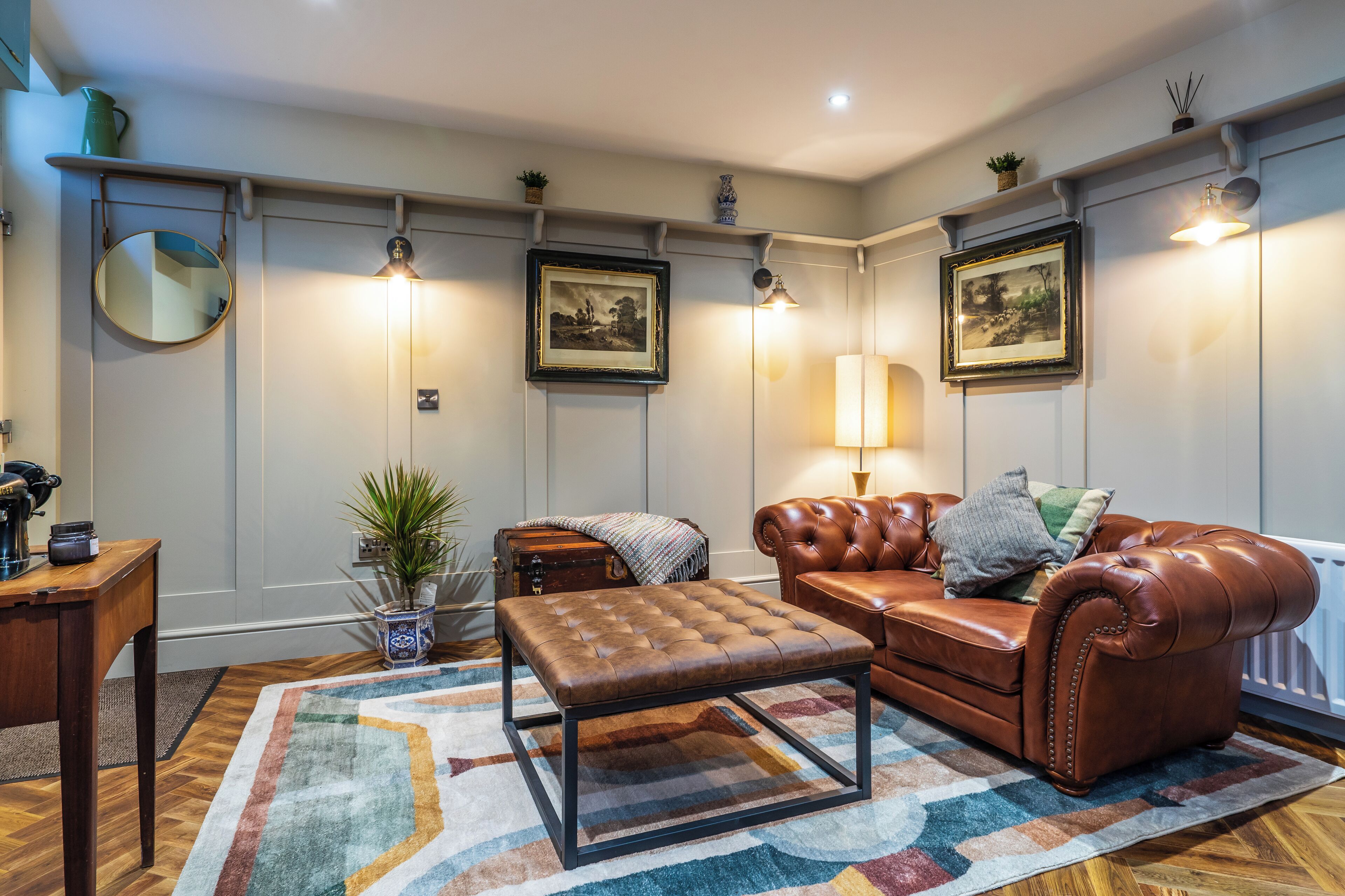 A living room with a brown leather sofa, a matching ottoman, a wooden coffee table, a patterned rug, and wall-mounted picture frames.