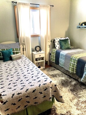 Une chambre avec deux lits, une table de chevet, une fenêtre avec des rideaux et une étagère fixée au mur.