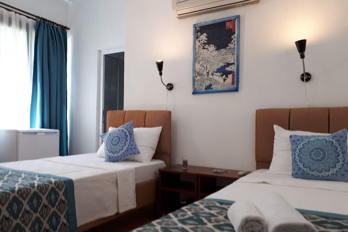 A hotel room with two beds, a nightstand, a wall-mounted lamp, and a painting.