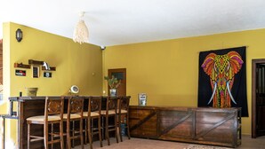 A dining area with wooden chairs and a central table, a wall-mounted light fixture, and a large tapestry. - San Simon Hotel (Kemer)