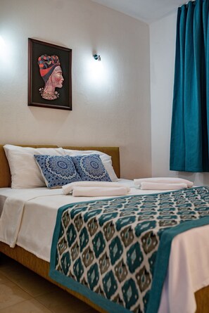 A neatly made bed with patterned bedding, a framed artwork above it, and a teal curtain on the window. - San Simon Hotel (Kemer)