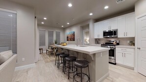 A modern kitchen with a central island, bar stools, stainless steel appliances, and white cabinetry.