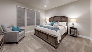 A bedroom with a large bed, a chair, a nightstand, and a lamp.