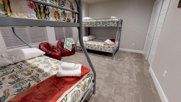 A dormitory room with bunk beds, a red bean bag chair, and a window with blinds.