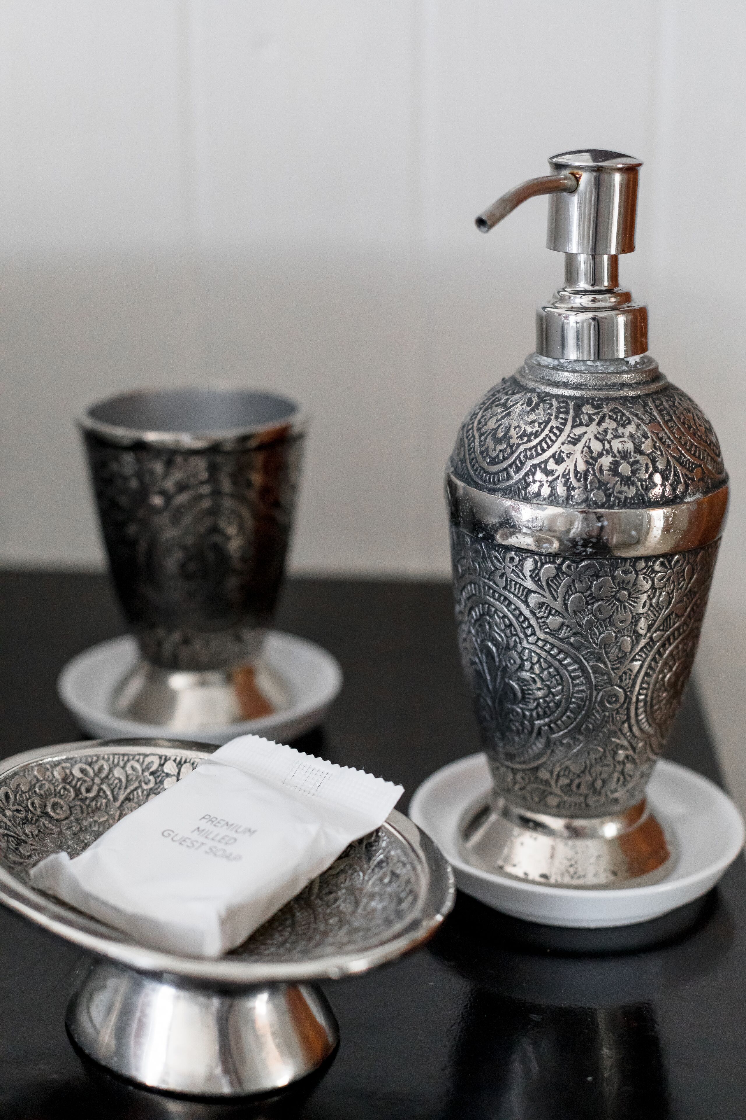 A silver tray with a soap dispenser and a cup on a black table.