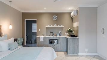 A modern bedroom with a large bed, a built-in kitchenette, a ceiling fan, and a clock on the wall.