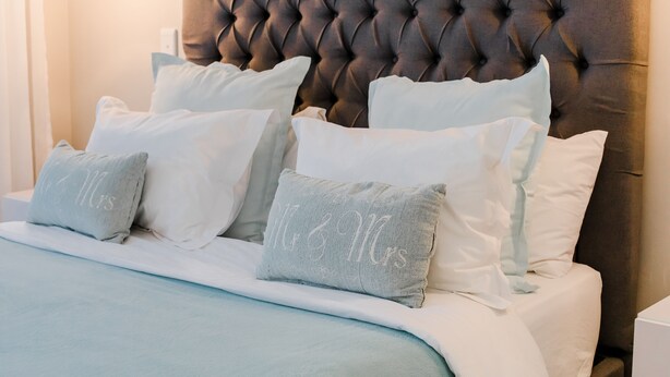 A bed with a tufted headboard, multiple pillows, and a light blue bedspread. - Wagtails Guest House (Gqeberha (Port Elizabeth))