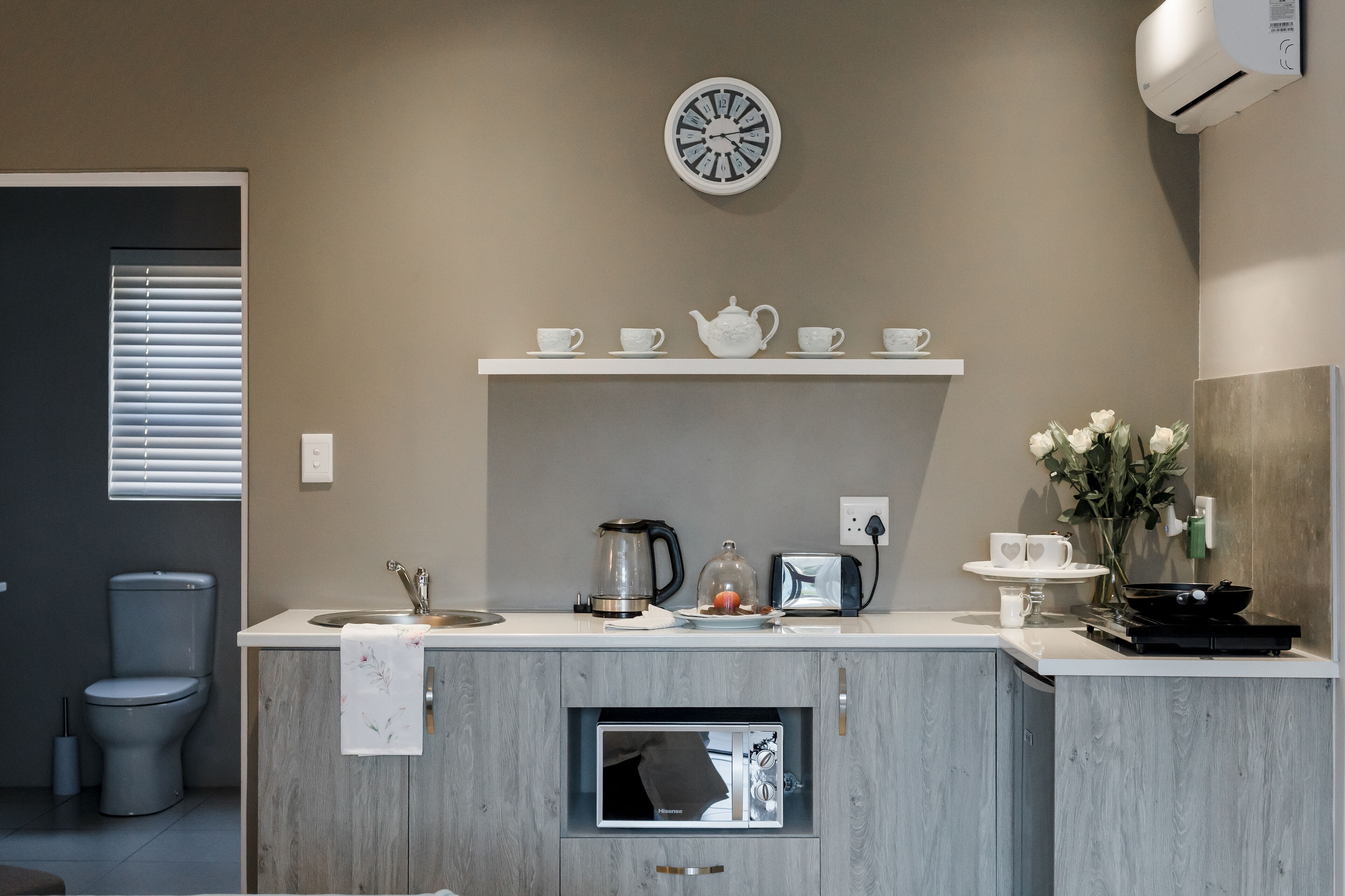 Una cocina moderna con microondas integrado, espacio para café y un reloj en la pared.