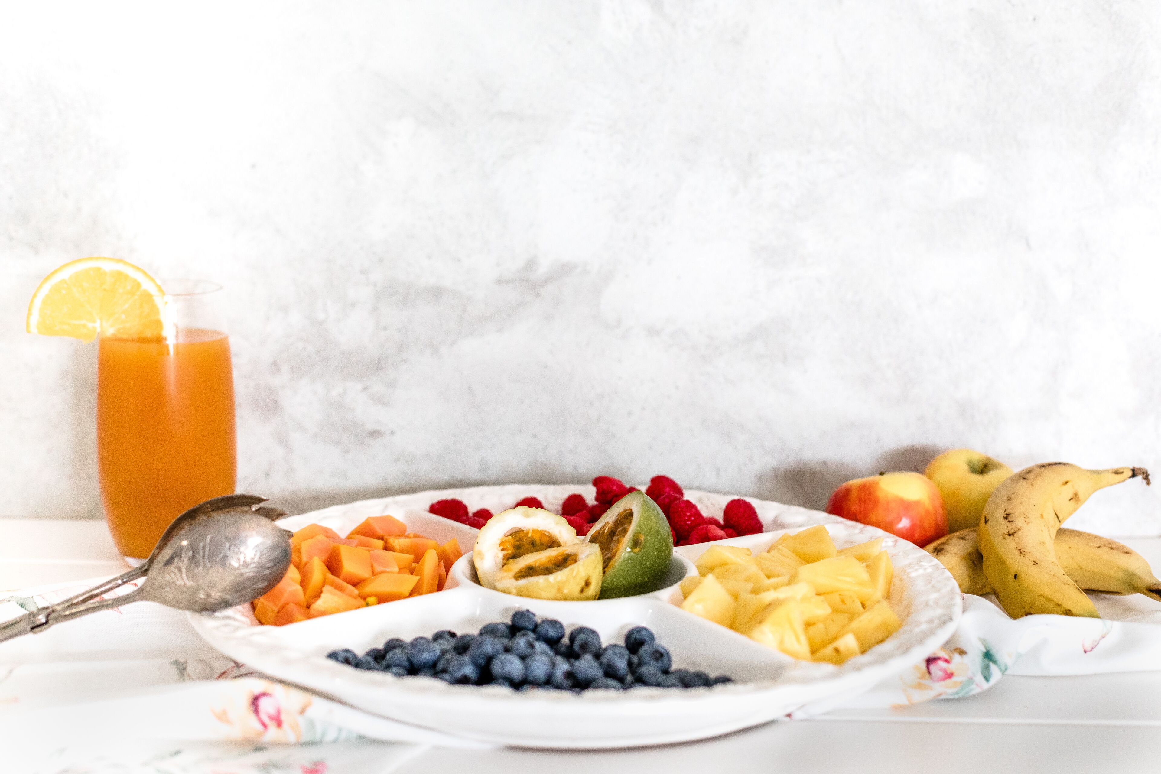 Uma tábua de frutas com diversas frutas e um copo de suco de laranja.