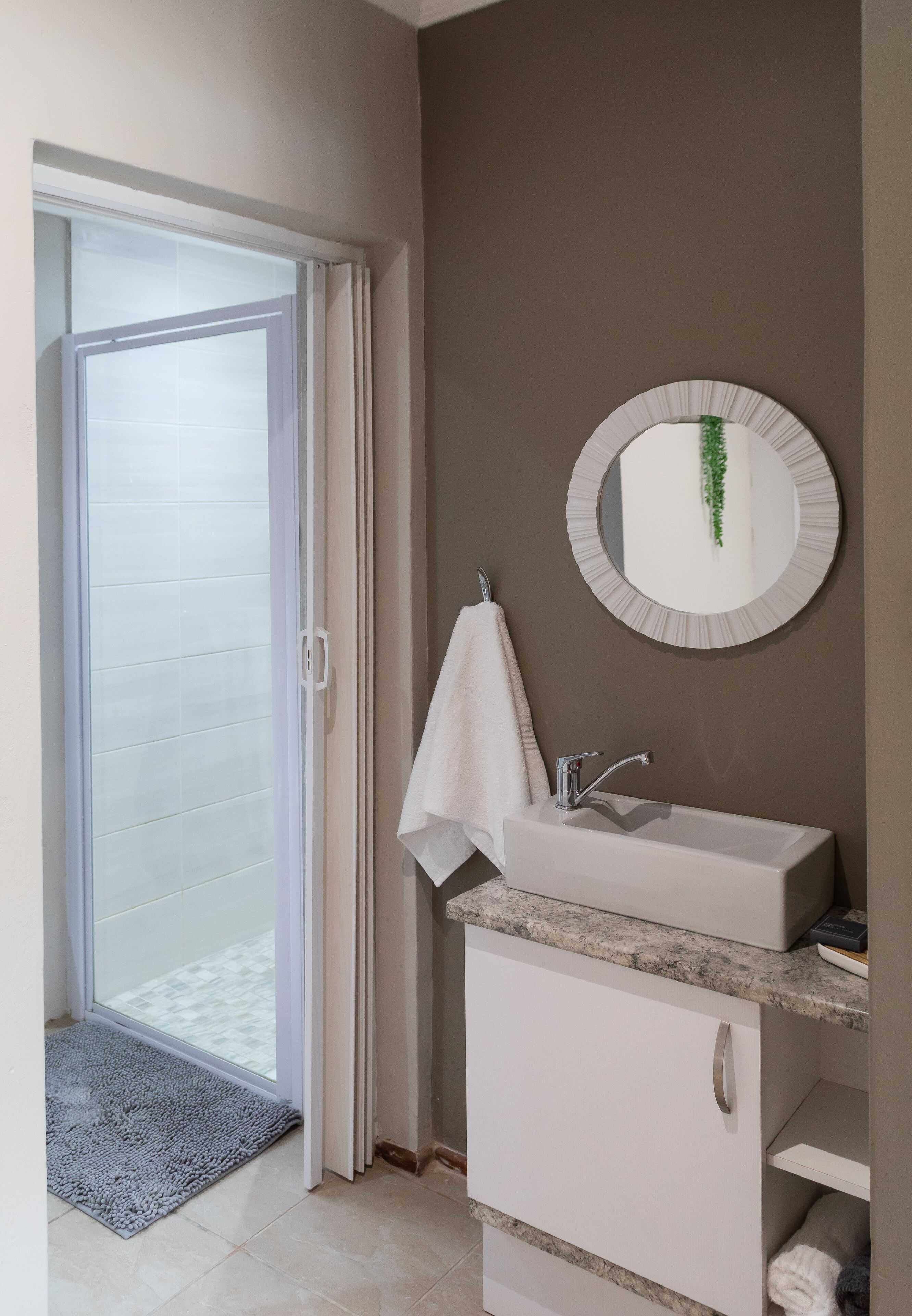 A bathroom with a white sink, a round mirror, and a towel hanging on the wall.