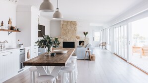 Eine moderne Küche mit einer Holztheke, weißen Barhocker, Pendelleuchten und einem Steinkamin.