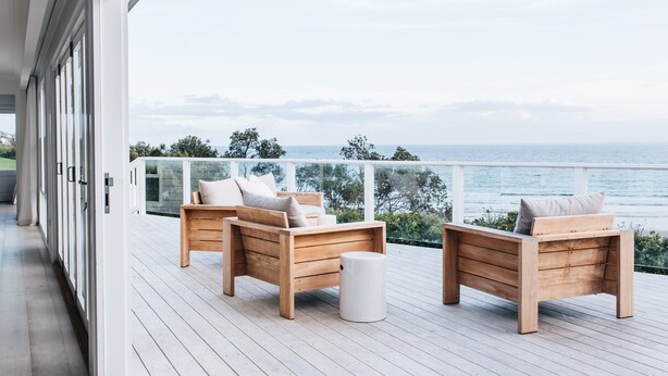 Eine Holzterrasse mit zwei Holzstühlen und einem kleinen weißen Tisch, mit Blick auf ein Gewässer.