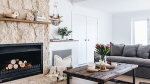 Ein Wohnzimmer mit Kamin aus Stein, einem grauen Sofa und einem Holztisch.