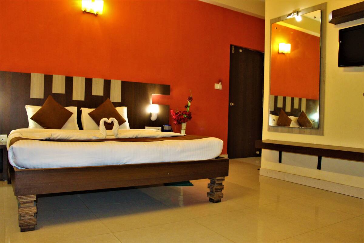 A neatly made bed with a wooden headboard, a bedside table with a vase of flowers, and a large mirror on the wall.