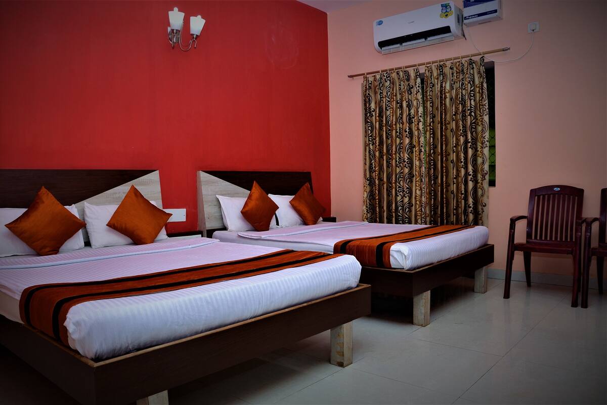 A hotel room with two beds, each with white linens and orange pillows, a wooden headboard, and a red wall.