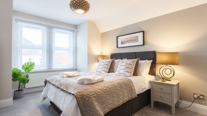 A bedroom with a bed, bedside table, lamp, and a window with blinds.