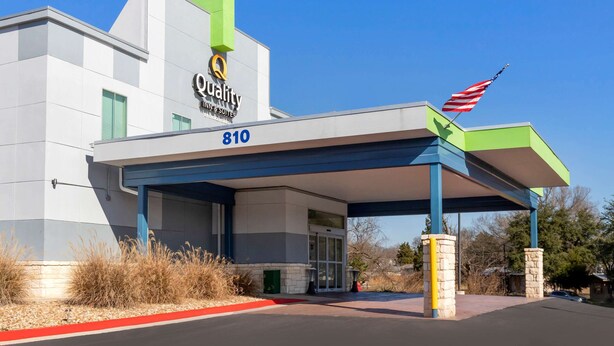 A modern building with a 'Quality' sign, a covered entrance, and an American flag.