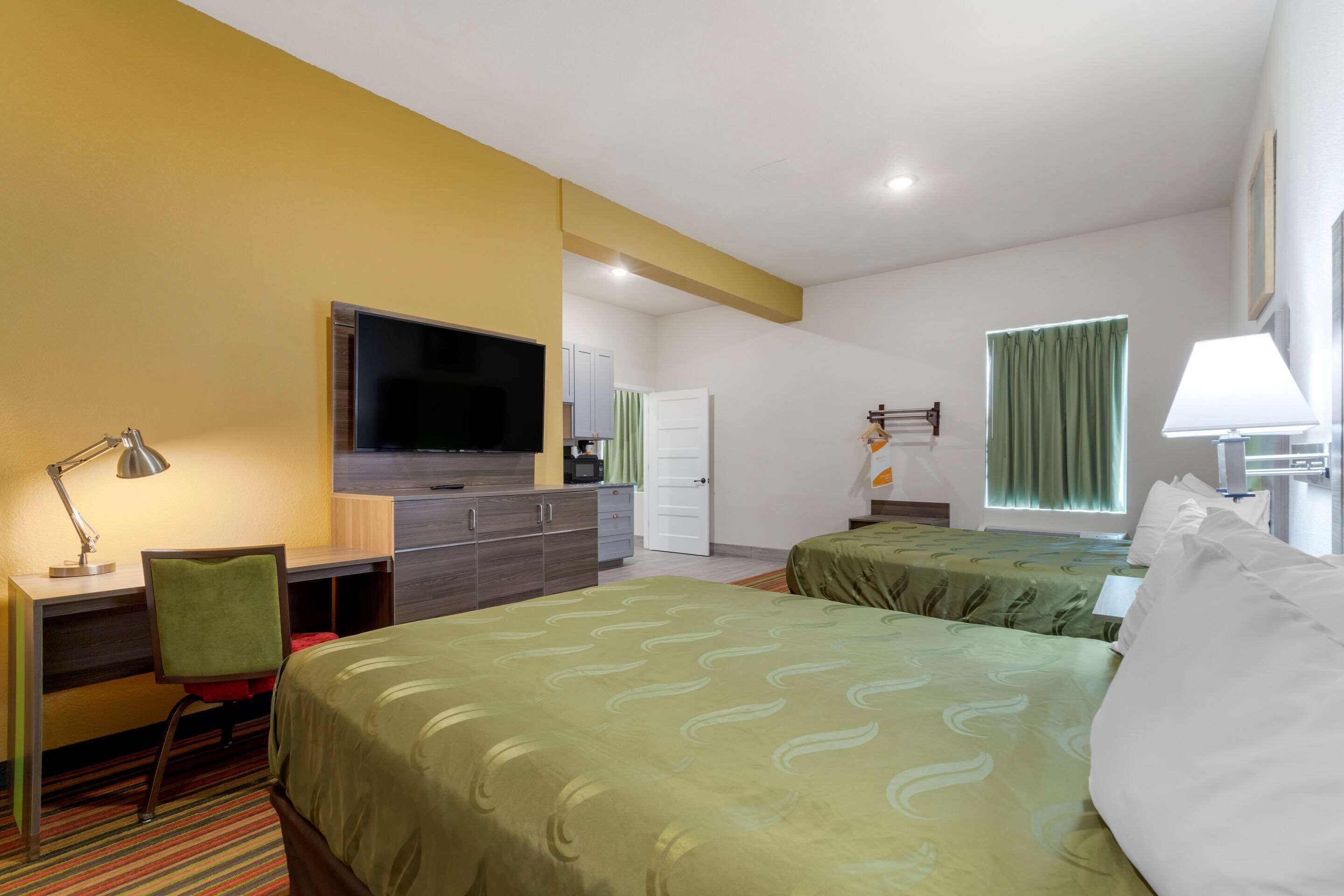 Una habitación de hotel con una cama, un escritorio, un televisor y un ventanal con cortinas.