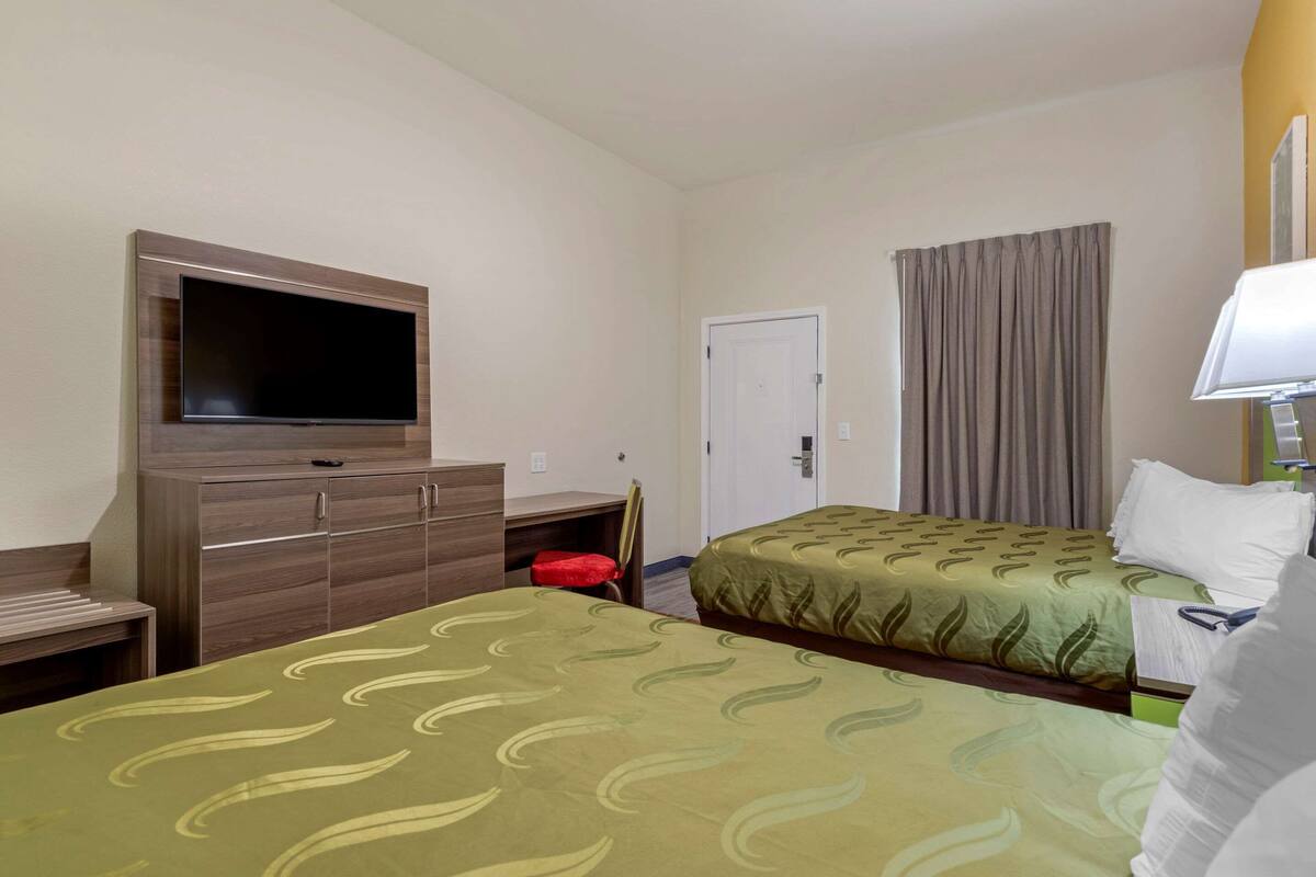 A hotel room with two beds, a television, a desk, and a door.