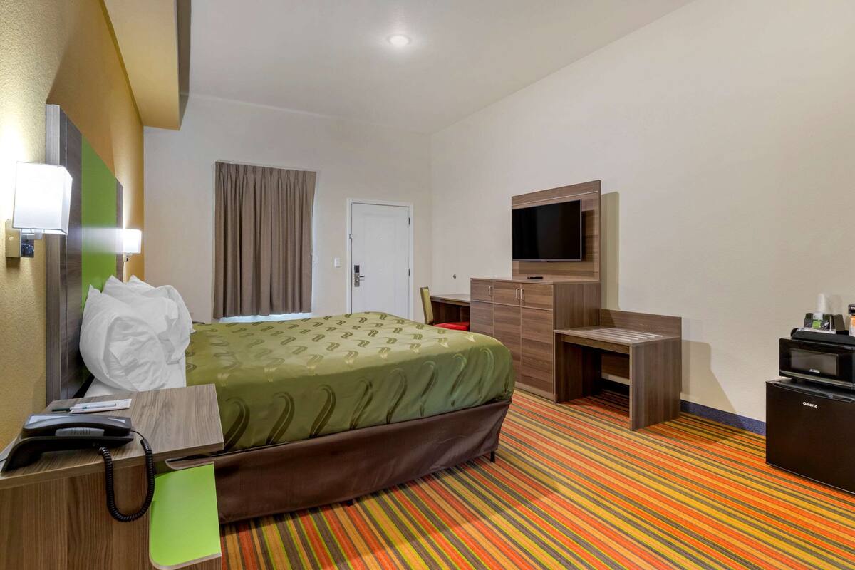 A hotel room with a bed, a desk, a television, and a minibar.