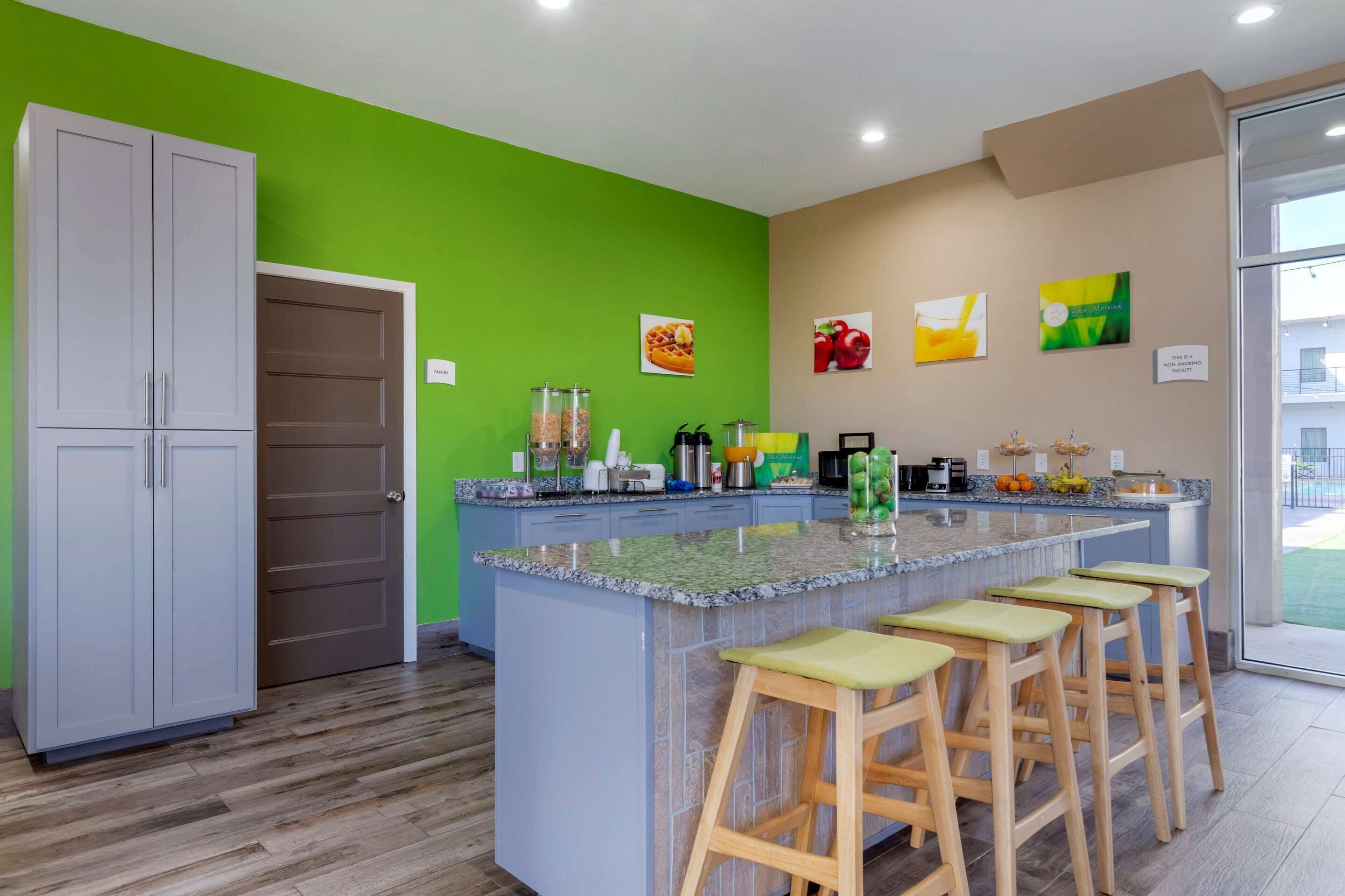 A kitchen with a green accent wall, a large island with stools, and various appliances.