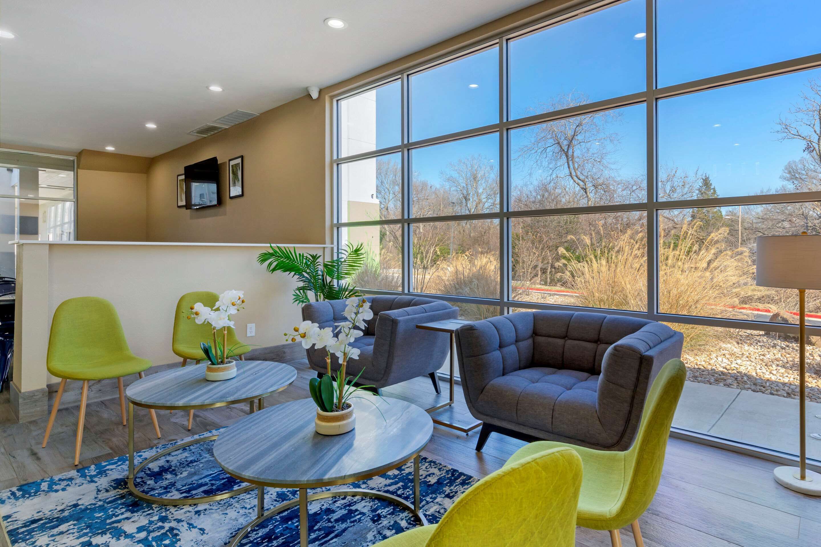 A modern hotel room with large windows, a seating area with chairs and a sofa, and a small table with a plant.